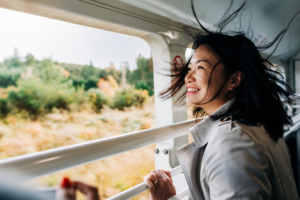 A passenger smiling in the wind on the open-air viewing carriage as countryside passes